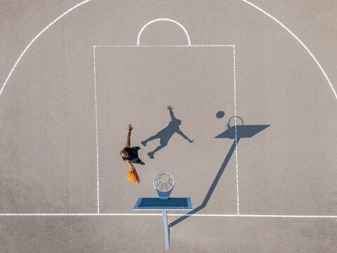 Aerial view of a basketball player jumping to shoot a ball towards the hoop on an outdoor court in Almere, Flevoland, Nederland.
