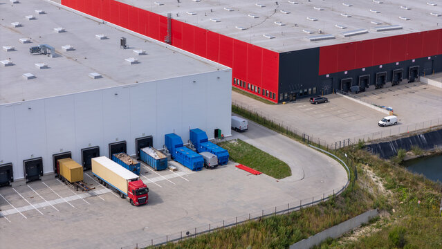 Aerial view of a modern logistics warehouse facility with loading docks, parked semi-trucks, and shipping containers in Gdansk, Poland.