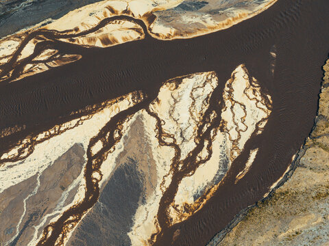 Aerial view of power plant ash disposal site with intricate braided channels of dark industrial sludge and light-colored sediment deposits in Poland.