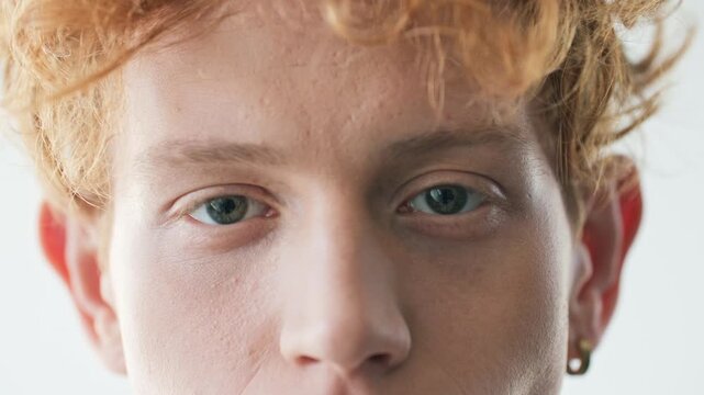Close up portrait Caucasian ginger man looking into camera with calm expression. Young male showing natural appearance and subtle confidence against clean background. Human emotions concept.