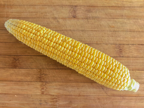 Top view of a single fresh yellow sweet corn cob isolated on a brown wooden background. Healthy organic food and agriculture concept.