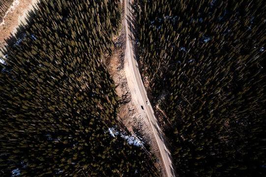 Aerial view of a winding road cutting through a dense pine forest in the Rocky Mountains, with patches of snow on the ground in Durango, Colorado, United States.