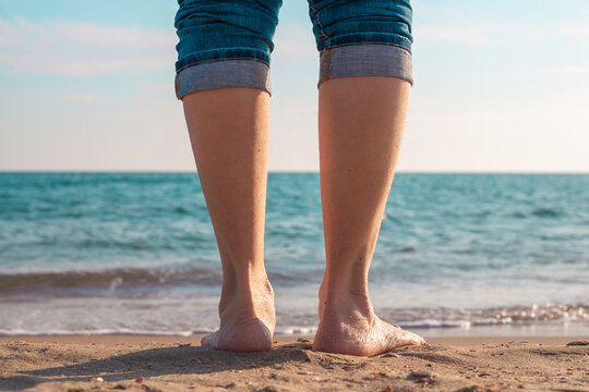 woman walking on the beach. Bare feet of a person stand on the wet sand of a beach at the edge of the sea. beach vacation, sea shore, summer relaxation.