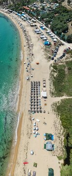 Aerial view of Sithonia beach with rows of umbrellas, tents, parked cars, and turquoise water along the sandy coastline in Halkidiki, Greece.