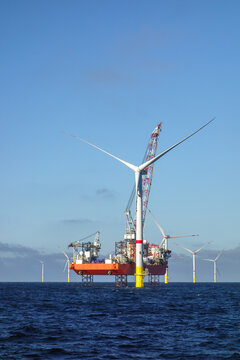 Offshore wind farm construction with a heavy-lift jack-up vessel installing a giant turbine. Renewable energy construction, offshore engineering