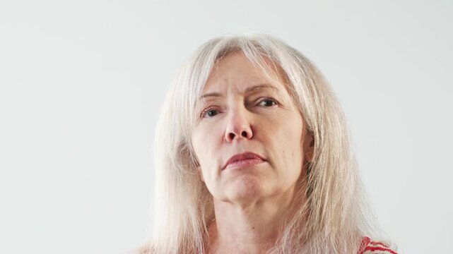 Senior Caucasian woman looking down at camera with serious expression. Portrait mature female showing disapproval concern or authority against clean background. Human emotions and attitude.