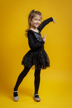 Smiling little girl in black dance costume posing on yellow background. Child portrait for dance, fashion and education.