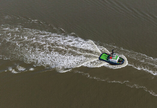 Aerial view of a small tugboat creating a white wake while navigating the waters of the Port of Antwerp, Kaai 102, Antwerpen, Vlaanderen, Belgium.