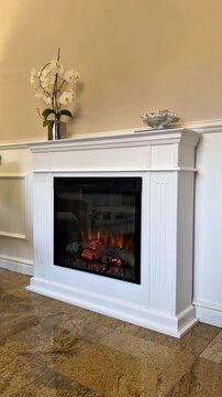 Modern white electric fireplace mantel with burning flames and white orchid in luxury living room interior, static shot