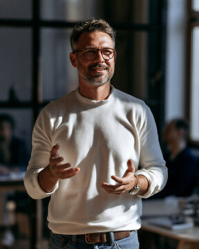 Confident man presenting in an office environment, gesturing with hands while communicating ideas, symbolizing expertise, leadership, and successful business engagement