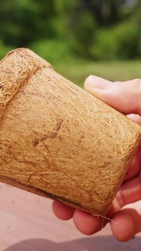 Vertical video. Hand Holds an Empty Coconut Fiber Pot Outdoors, Biodegradable Planting Container for Sustainable Gardening and Environmentally Responsible Cultivation