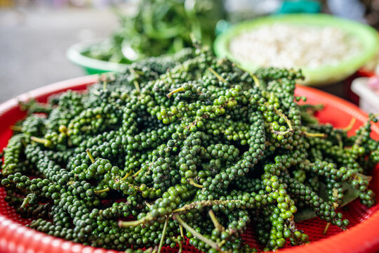Plastic basket filled with pile of fresh green peppercorns on stem, unripe Piper nigrum vine berries, street food market selling mild green peppercorns, culinary spice highly prized in Southeast Asia.