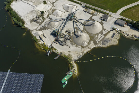 Aerial view of a sand and gravel extraction plant with conveyor belts, large piles of sand, and a floating solar panel array on the water in the Netherlands.