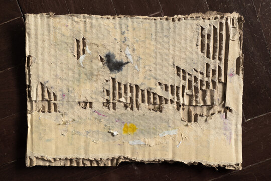 Weathered Corrugated Cardboard with Peeling Texture on Dark Parquet Wood Floor