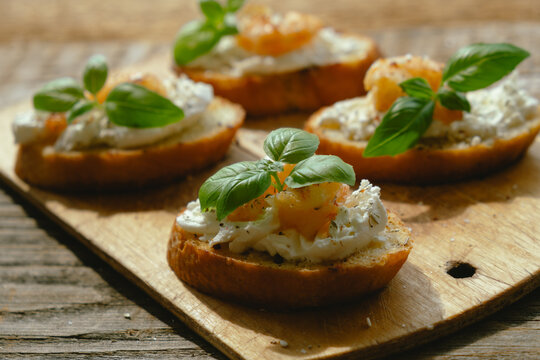 Bruschetta or crostini. Toasted bread slices with with cream cheese, shrimp and fresh basil leaves on wooden board