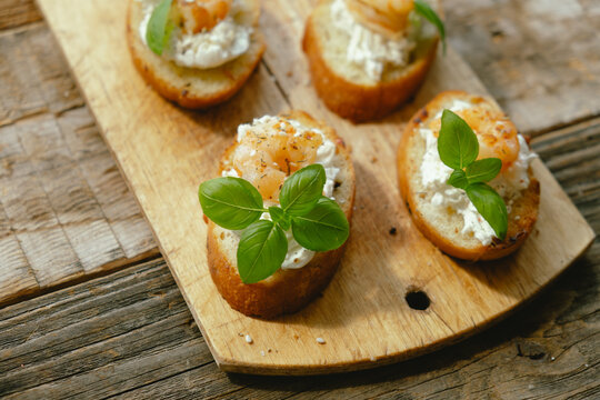 Bruschetta or crostini. Slices of toasted bread with feta, shrimp and fresh basil on wooden board.