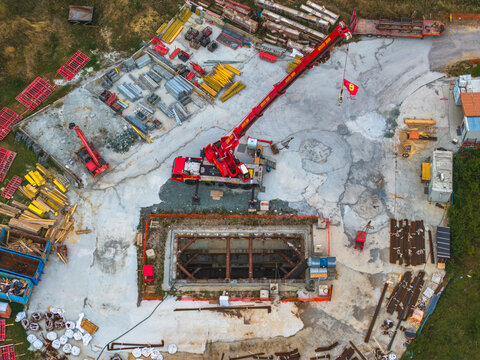 Aerial view of a red mobile crane positioned at a construction site with an excavation pit and various building materials in Serravalle Scrivia, Piedmont, Italy.