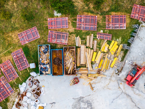 Aerial view of construction site with red formwork panels, wooden beams, dumpsters, and a red construction vehicle in Serravalle Scrivia, Piedmont, Italy.