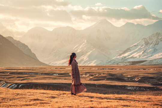 Asian Woman Standing in Golden Steppe Landscape with Snowy Mountain Range at Sary Jaz Valley