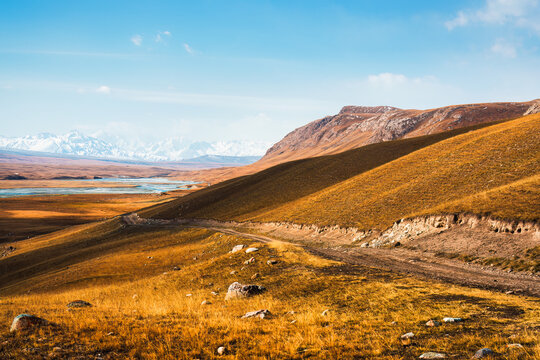 Dirt Road Winding Through Golden Grassland Toward Snow Capped Mountain in Sary Jaz Valley Central Asia