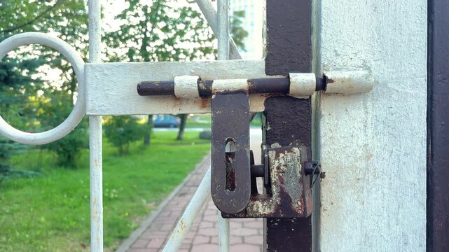 Old rusty barrel bolt and latch mounted on a weathered metal fence, security hardware, aged texture, industrial detail.