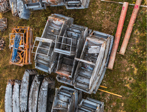 Aerial view of construction materials including metal frames and pipes stored on a grassy site in Serravalle Scrivia, Piedmont, Italy.