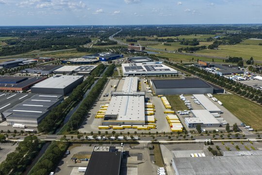 Aerial view of the DHL logistics facility featuring large warehouses, rows of yellow delivery trucks, and surrounding industrial infrastructure in Zwolle, Overijssel, Netherlands.