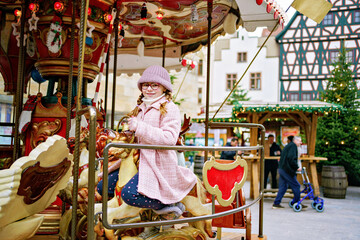 Little school girl riding on a merry go round carousel at Christmas funfair or market, outdoors. Happy child having fun on traditional family xmas market in Germany © Irina Schmidt