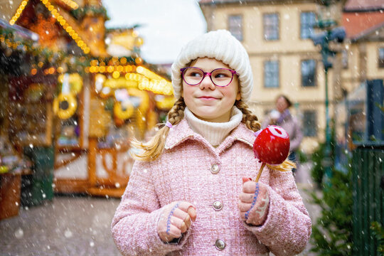 Little cute kid girl eat sweet sugar covered red candy apple on Christmas market. Happy child on traditional Xmas fair in Germany.