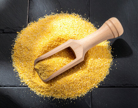 Hand-carved wooden spoon resting in a pile of golden cornmeal on a matte black slate tile with soft shadows.