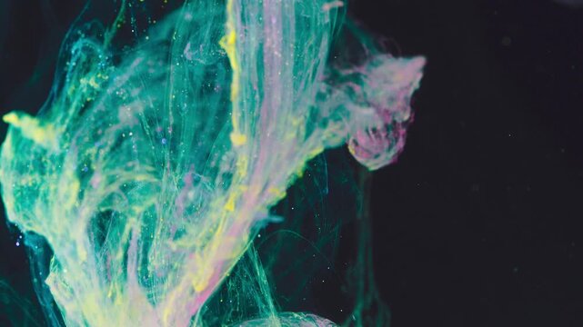 Close-up of colorful ink plumes diffusing in dark liquid with teal magenta and yellow swirls