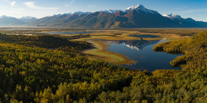 Alaskan snow-capped mountains in distance during fall with rising sun on the valley and lake reflection