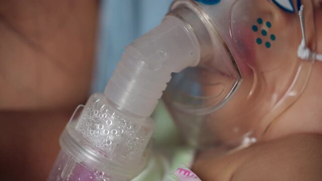 Mother holds her sick baby boy during nebulizer treatment in hospital, showing parental support, pediatric respiratory care, inhalation therapy, breathing difficulty, and recovery.