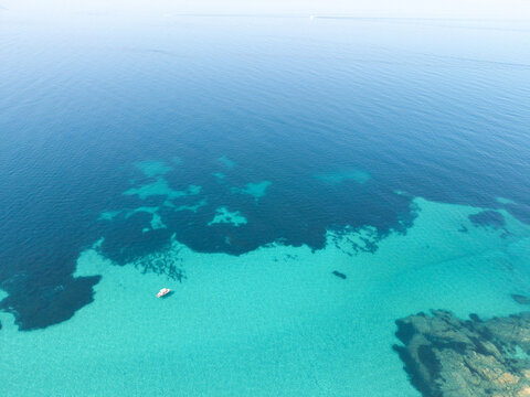 Aerial view of a small boat floating in the crystal clear turquoise waters of Nisis Dhiaporos, showcasing the rocky seabed and vibrant blue sea in Halkidiki, Greece.