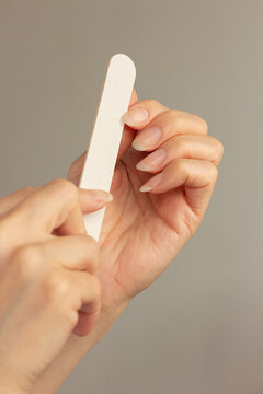 Close up of woman filing her healthy natural long fingernails with a nail file. Concept of manicured hands, home beauty routine, and self care.	
