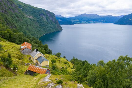 Aerial view of Ospahjellen featuring traditional wooden houses on a lush green hillside overlooking the deep blue waters of the fjord in Liabygda, More og Romsdal, Norway.