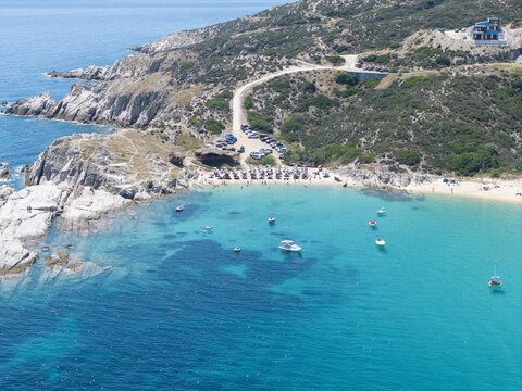 Aerial view of Kriaritsi Beach with turquoise waters, sandy shore, umbrellas, boats, and rocky coastline in Greece.
