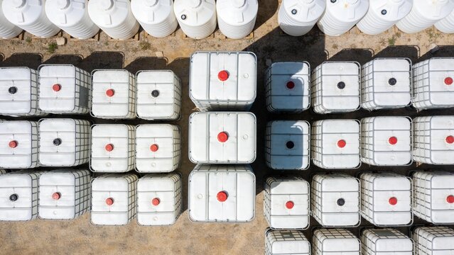 Factory warehouse exterior featuring stacked white liquid containers for industrial chemical handling.