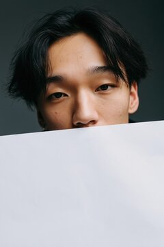 Close frontal portrait of young man holding white paper sheet for minimal portrait background or social media header