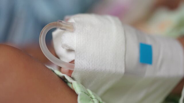 Close-up of an infant hand with an IV catheter secured by medical gauze during hospital treatment, representing pediatric care, intravenous therapy and childhood illness.