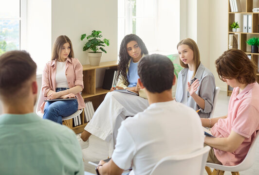Students discussion group in classroom meeting seminar. Young people sit in a circle sharing ideas and notes in a bright modern room. Peers learn. Concept teamwork communication and learning.