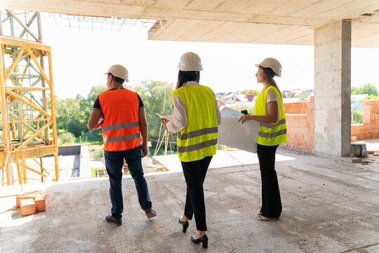 Worker and managers perform walkaround of building. Builder and female project employees analyse layout walking at unfinished floor against crane