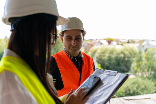 Builder and managers use smartphone to analyze building layout. Foreman and engineer prepare to begin reviewing areas standing near outside view