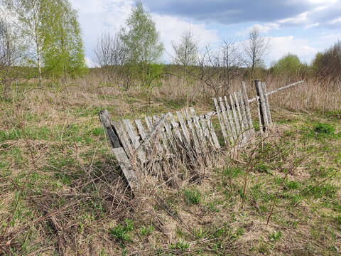 A weathered wooden fence stands amidst dry grass under a partly cloudy sky.
