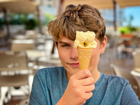Cheerful laughing preteen boy eating multicolored ice cream in a waffle cone. Cool in the summer heat.Sweet snack for children. Happy child.