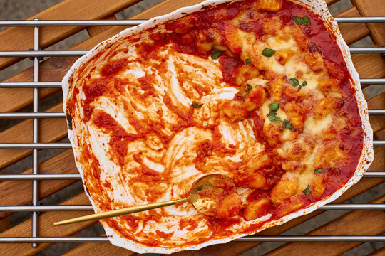 Leftover gnocchi with tomato sauce, cheese and basil remain in ceramic baking dish with serving spoon