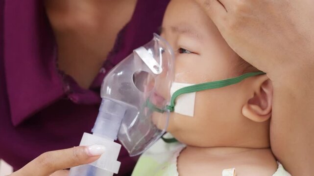 Sick baby boy wears a nebulizer mask during breathing therapy in hospital, depicting pediatric healthcare, asthma management, respiratory illness, medication, and recovery care.