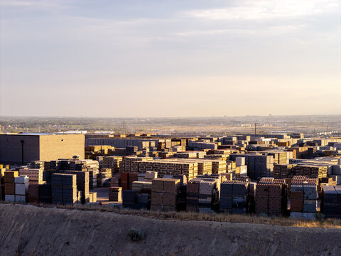 Aerial view of stacks of construction materials including bricks, pavers, and cinder blocks arranged in an industrial yard during golden hour in Bluffdale, Utah, United States.