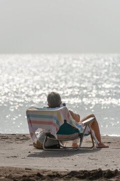 Vertical back view of person relaxing on beach chair by the sea