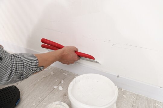 Worker plastering white wall with putty knife indoors, closeup